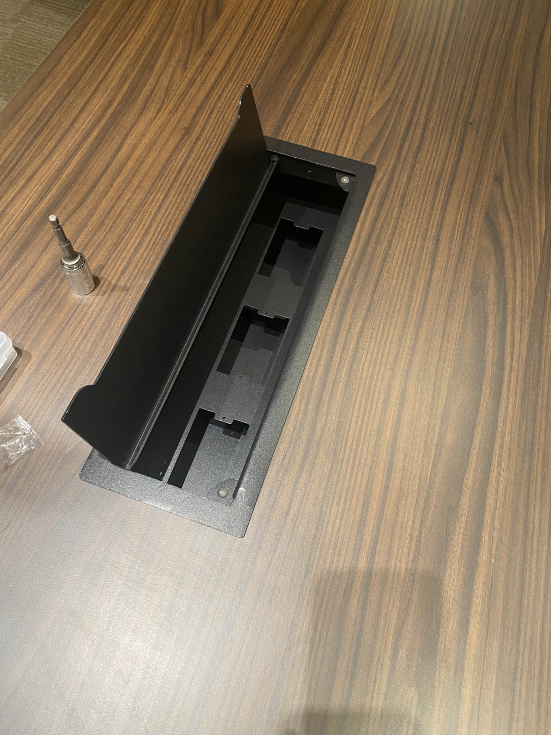 Detalle de una mesa con acabado de madera y una canaleta negra integrada en la cubierta.