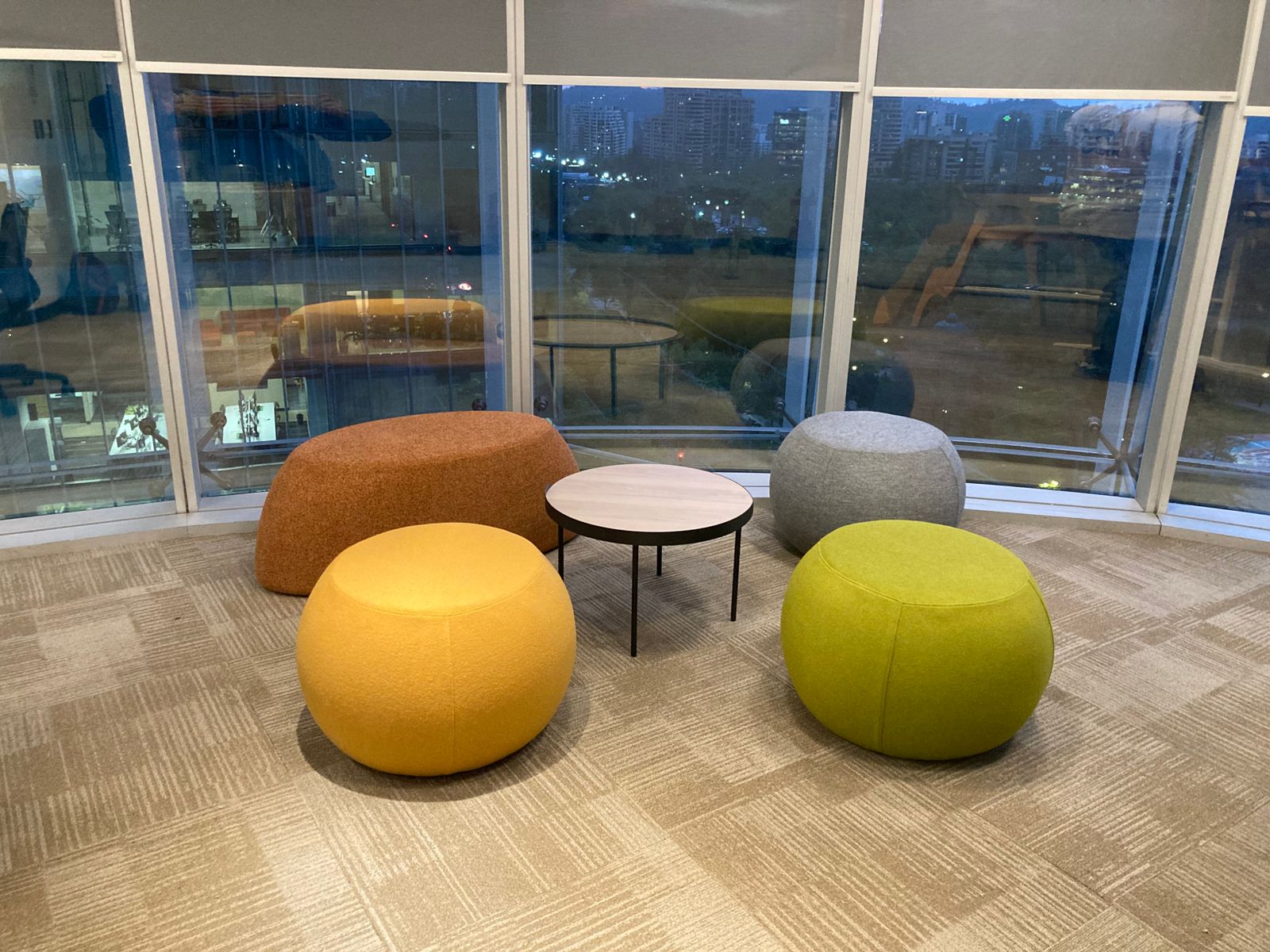 Zona de encuentro con asientos tapizados de colores y una mesa circular junto a ventanales.