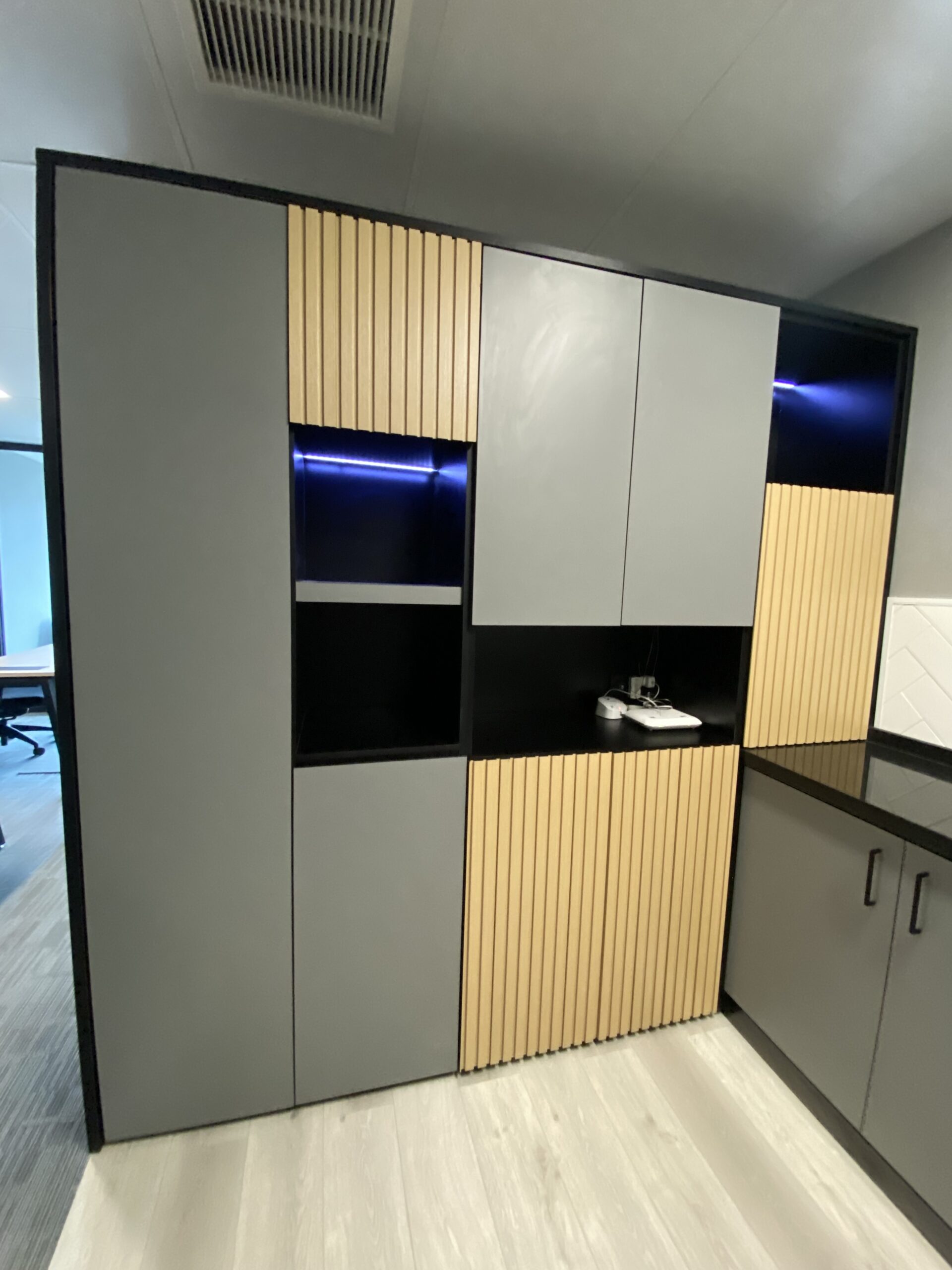 Mueble alto con puertas grises y de madera clara, nichos oscuros e iluminación azul.