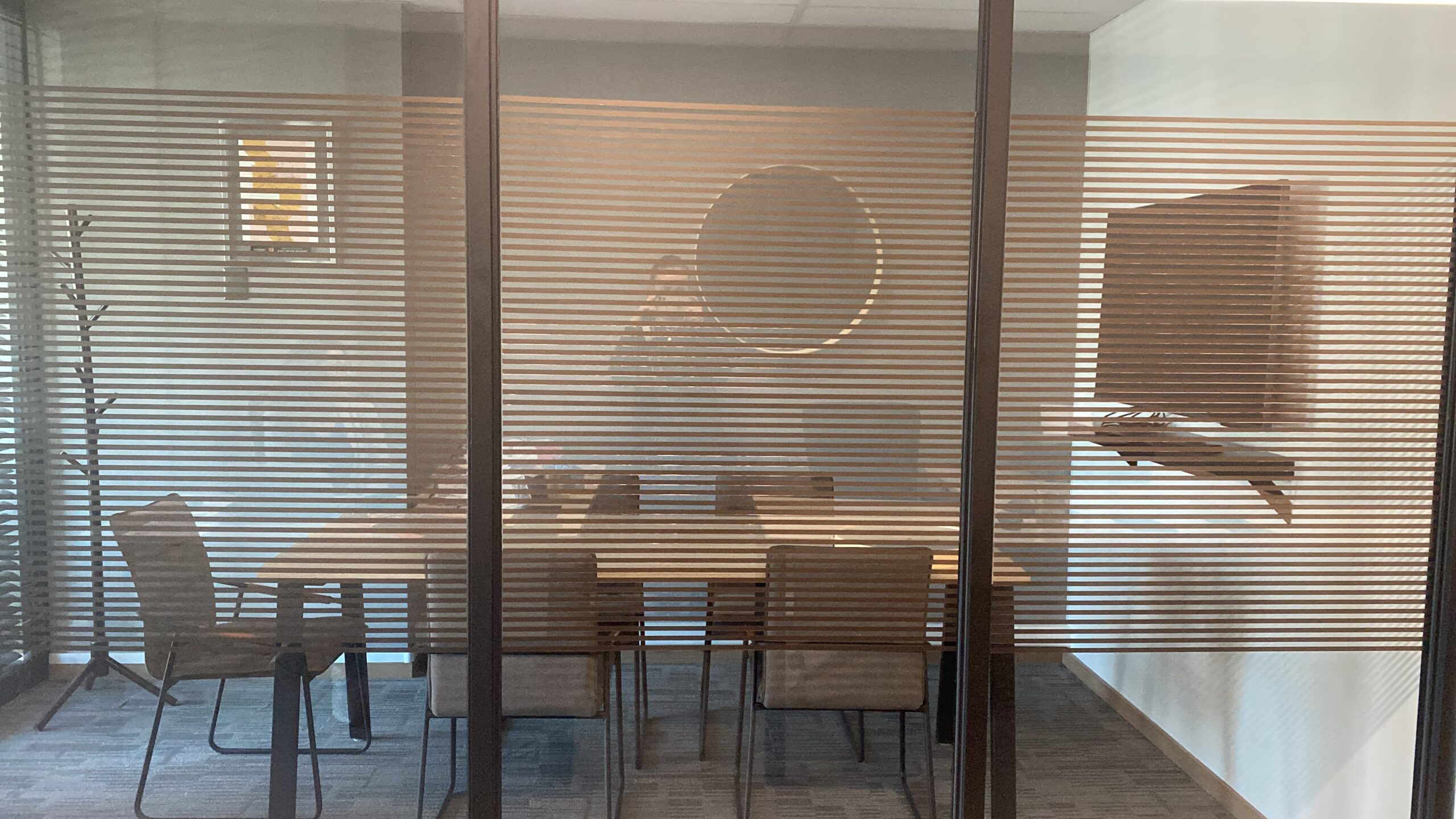 Sala con mesa y sillas vista a través de una mampara de vidrio con líneas horizontales.