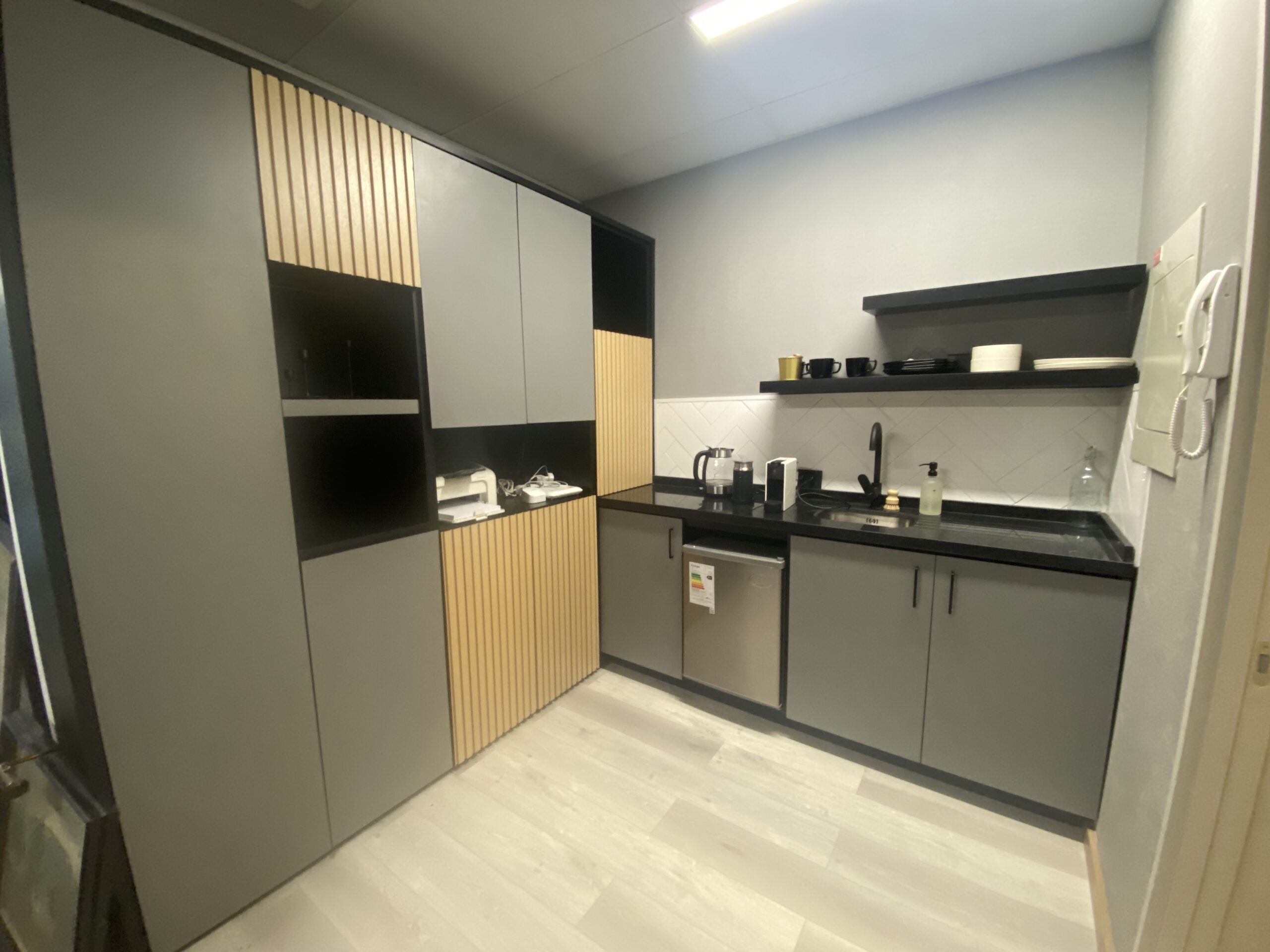 Muebles de cafetería en tonos gris y madera clara, con cubierta oscura y lavaplatos.