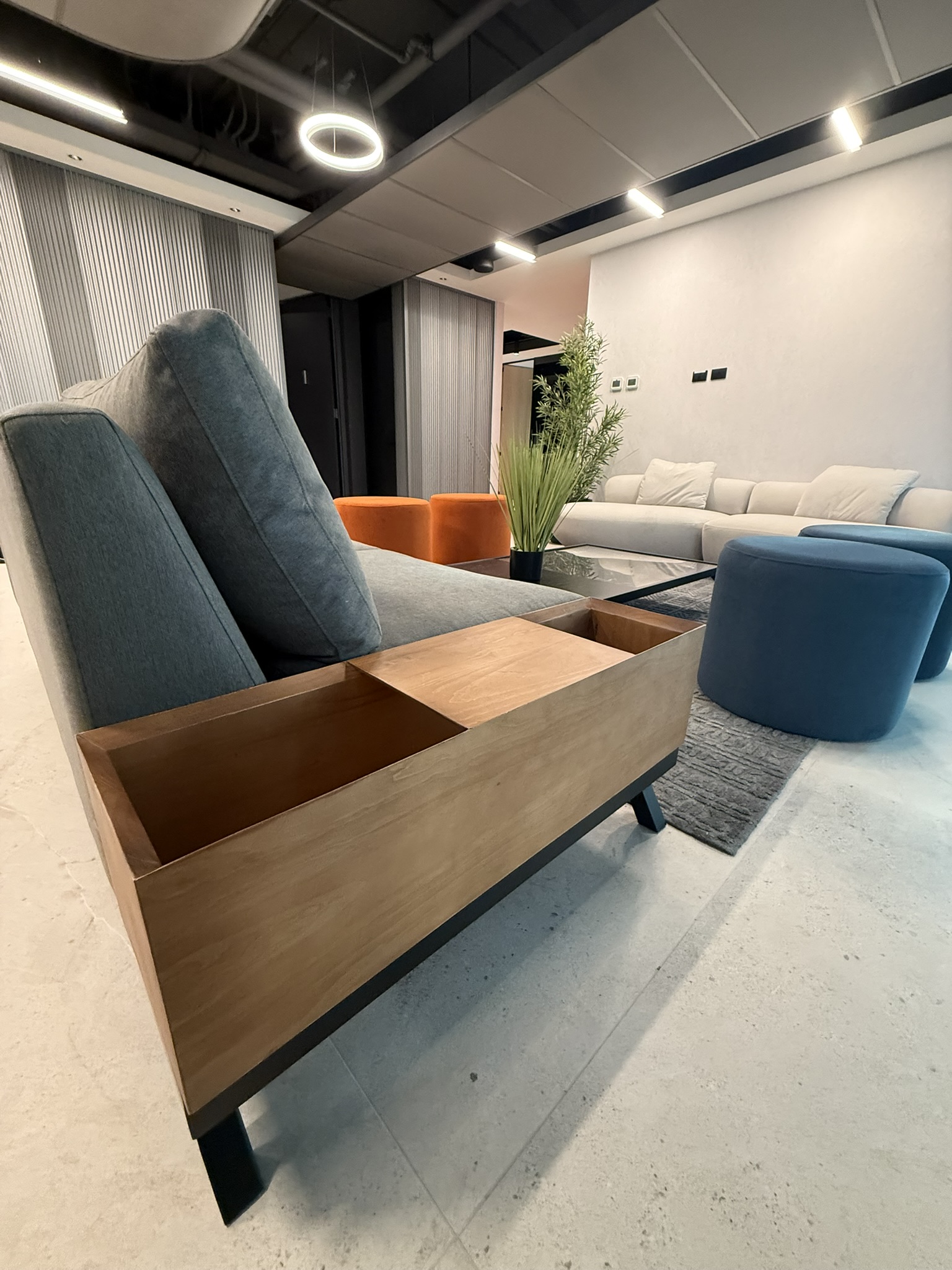 Detalle de un sillón con respaldo tapizado azul y estructura de madera junto a una mesa.