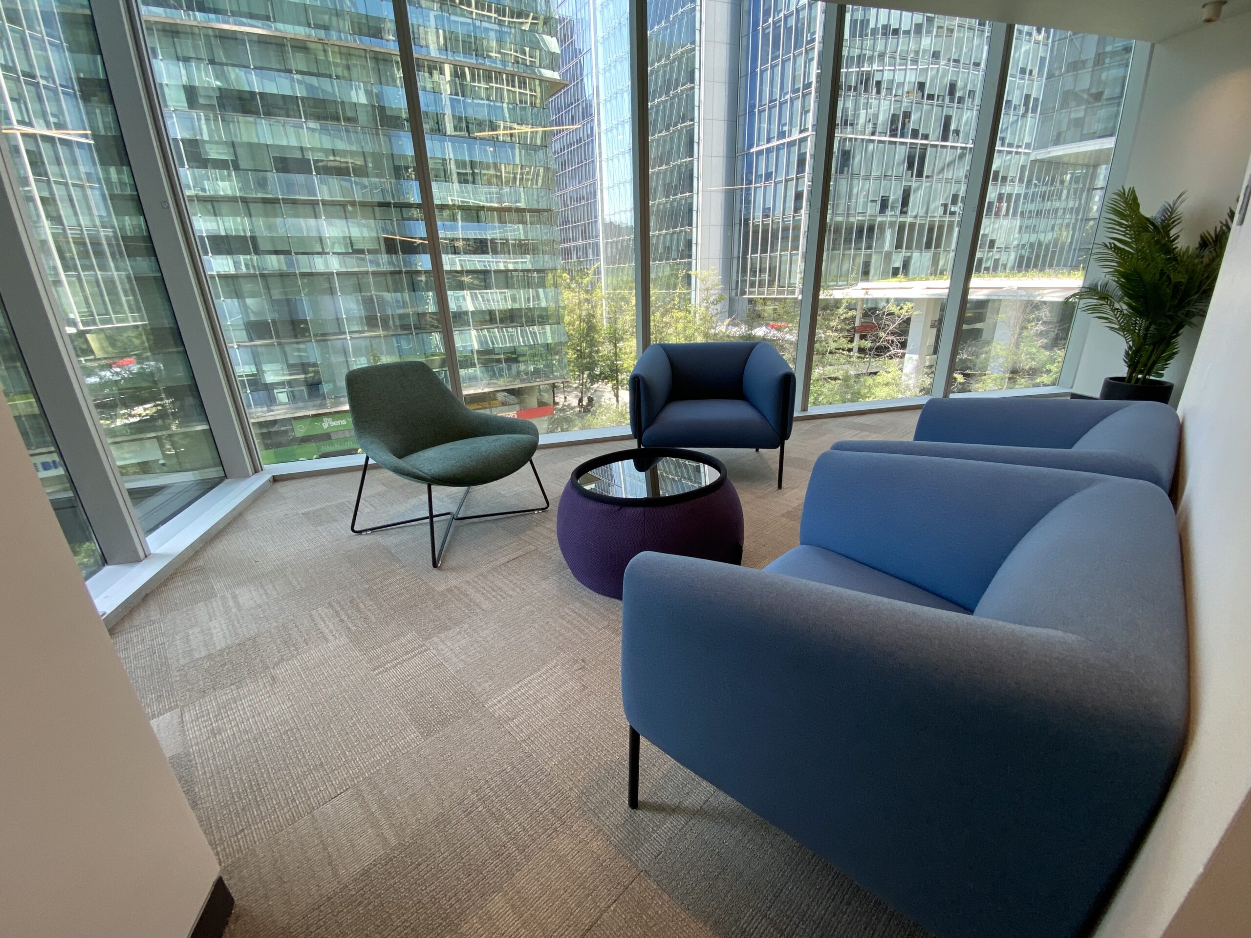 Sillones azules y una silla verde alrededor de una mesa circular junto a ventanales.